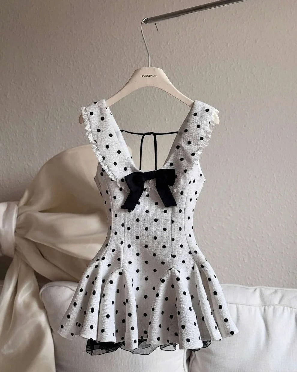 Polka dot dress with a black bow on a hanger against a neutral background