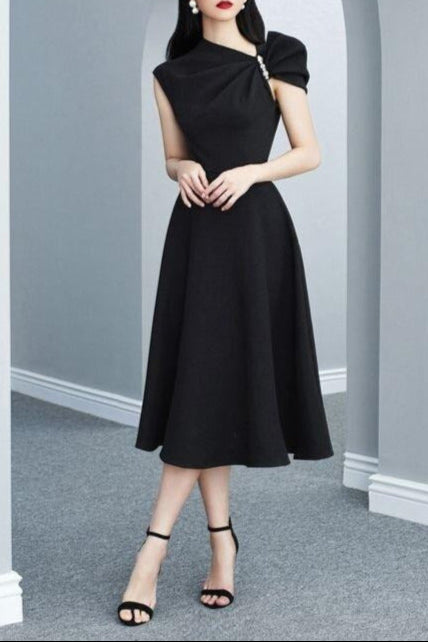 Woman wearing a black dress standing in an archway with gray walls and floor.