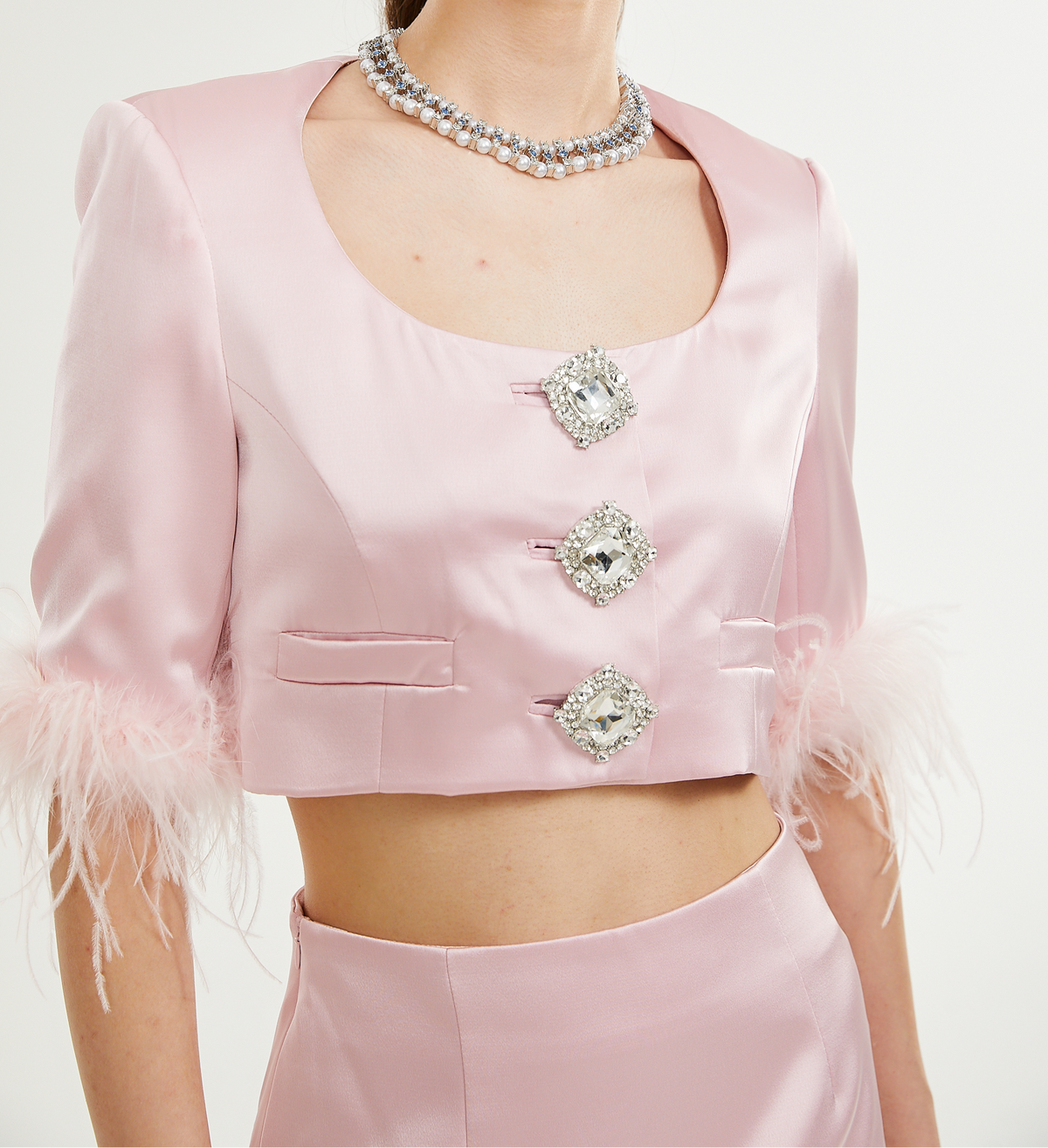 Woman wearing a pink outfit with feather details and embellishments on a white background