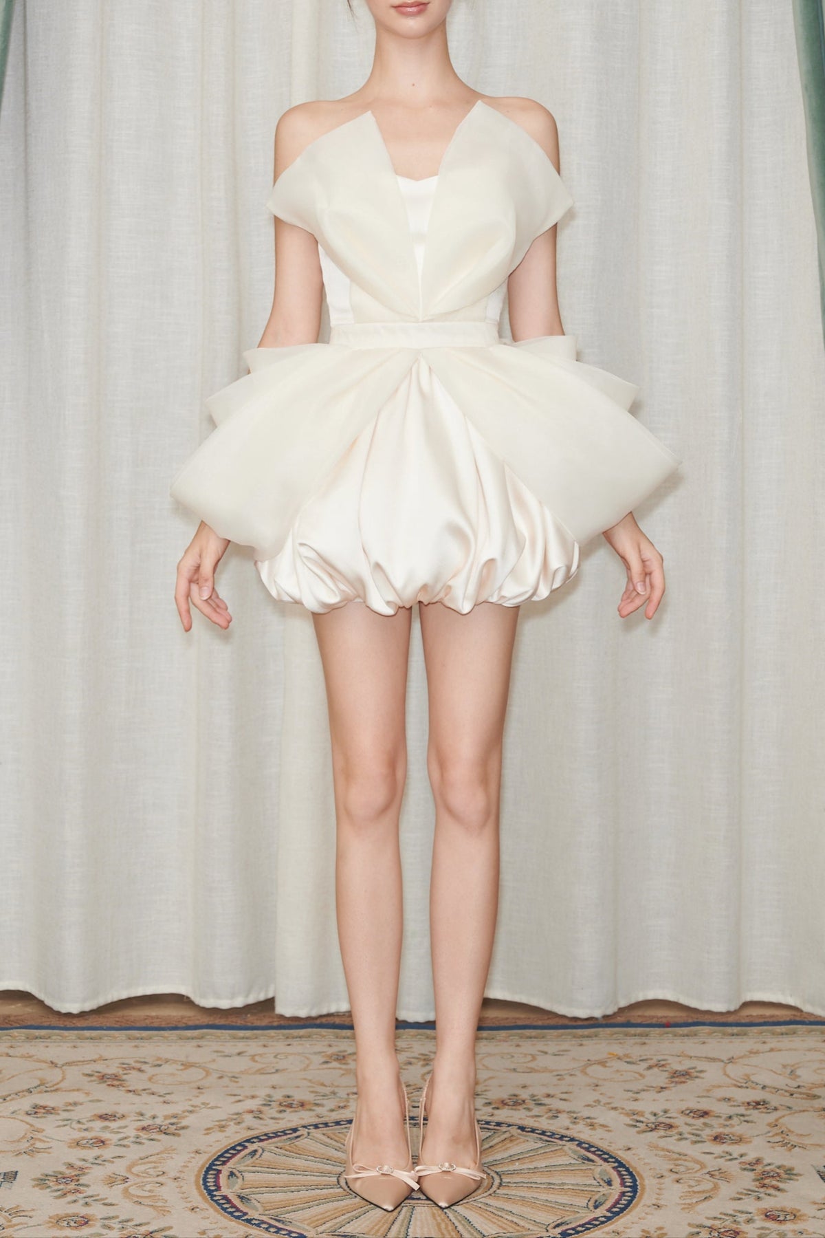 Model wearing a white dress with a ruffled skirt against a curtain backdrop