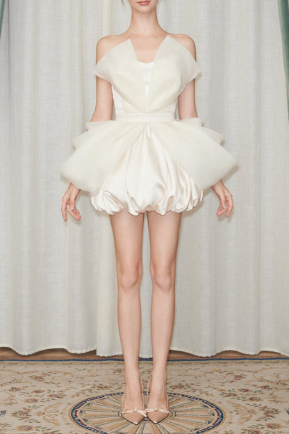 Model wearing a white dress with a ruffled skirt against a curtain backdrop