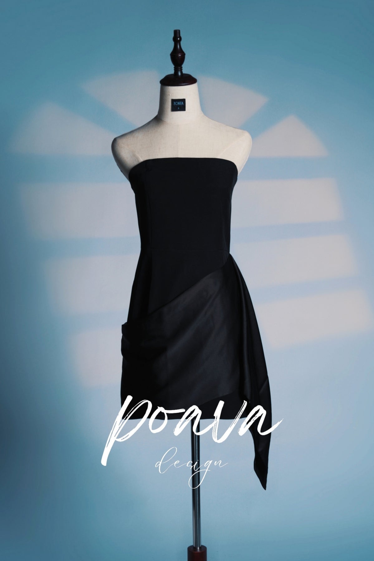 Black satin mini dress with a draped skirt and bandeau neckline, displayed on a mannequin against a blue background.