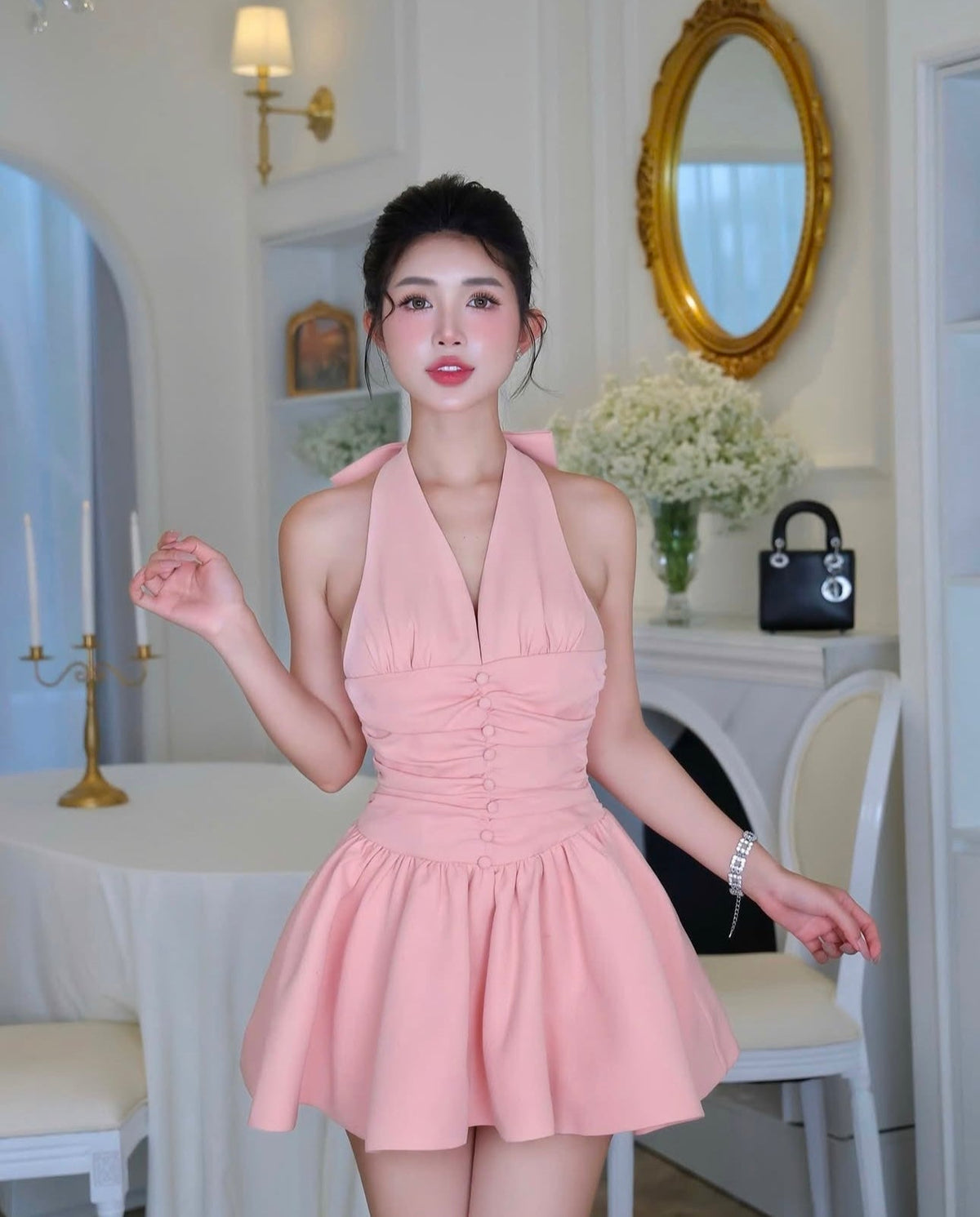 Woman in a pink dress standing in a well-lit room with decorative elements.