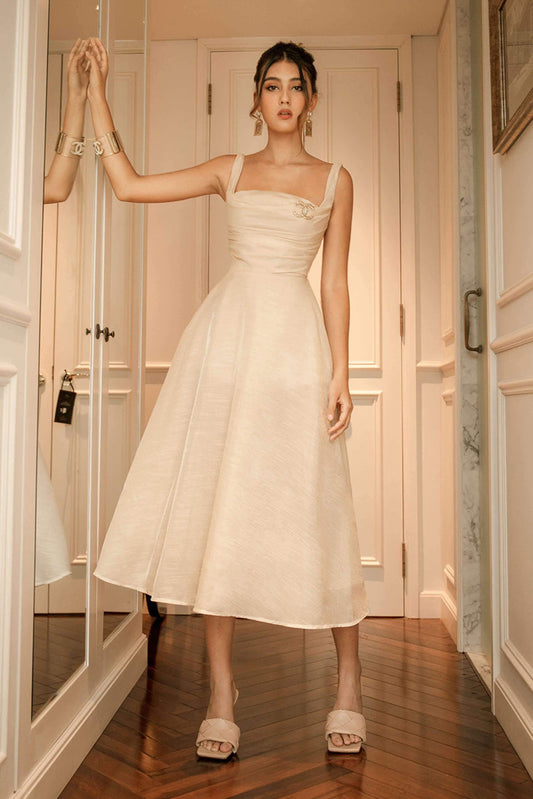 Woman in a white dress standing in a room with wooden floor and white walls.