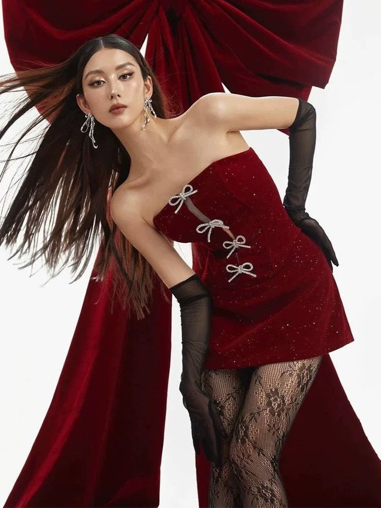 Woman in a red dress with black gloves and stockings posing against a red curtain.
