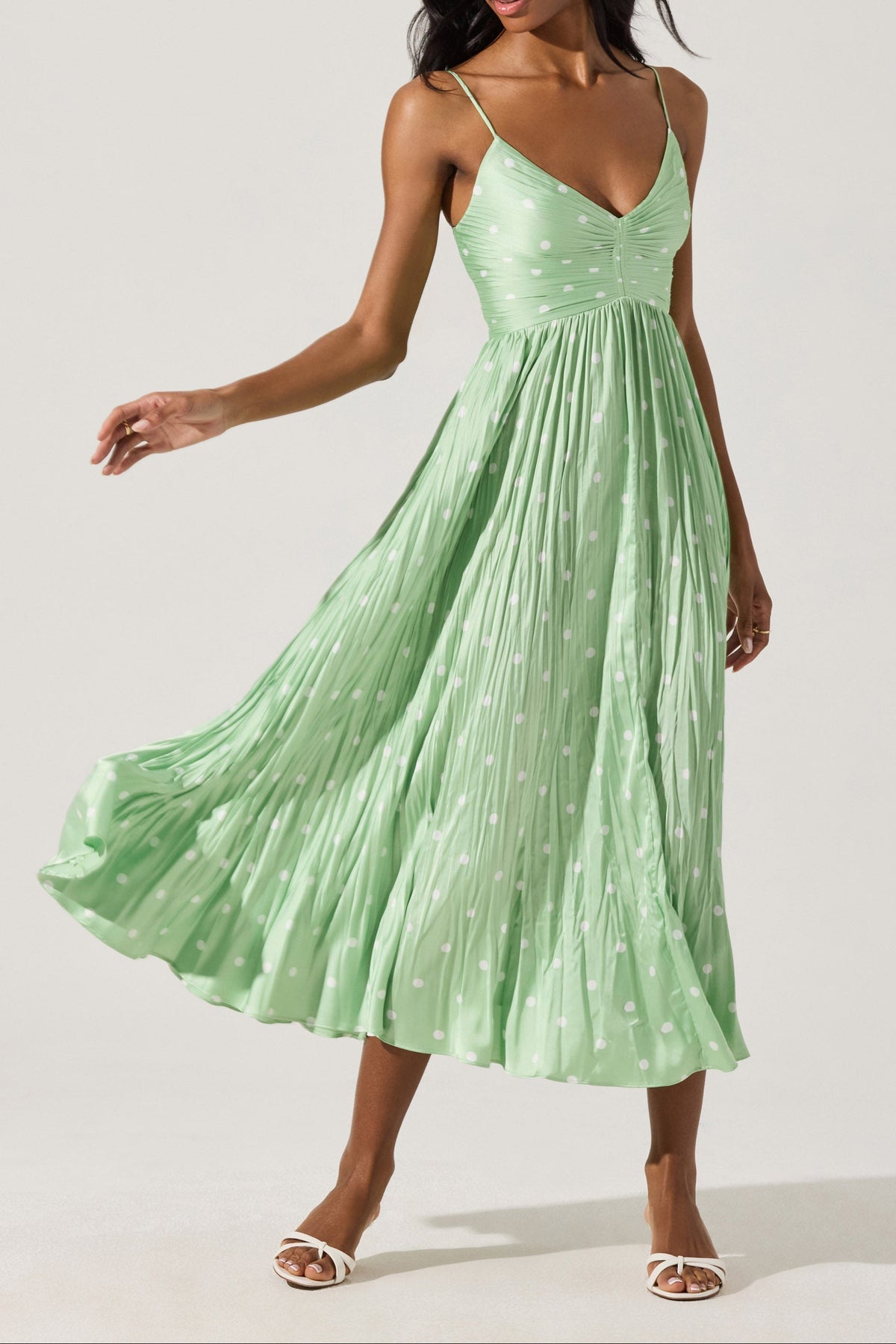 A woman wearing a green pleated midi dress with a sweetheart neckline and adjustable spaghetti straps.