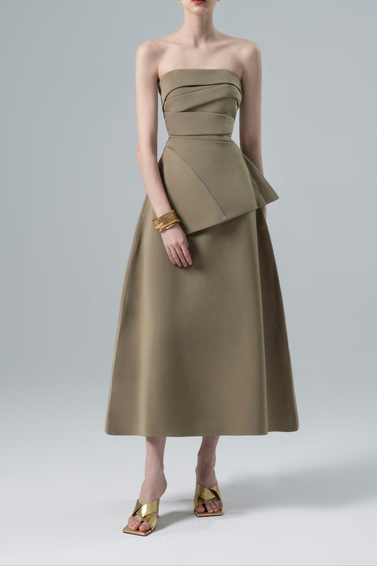 A woman standing wearing a green, floral print strapless top with draped detailing and a fitted waist, paired with a flare bottom skirt.