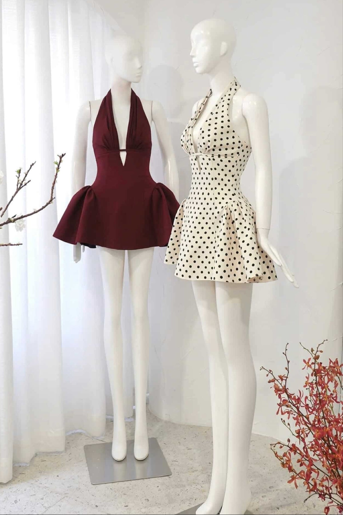 Two mannequins wearing dresses in a display setting with decorative elements.