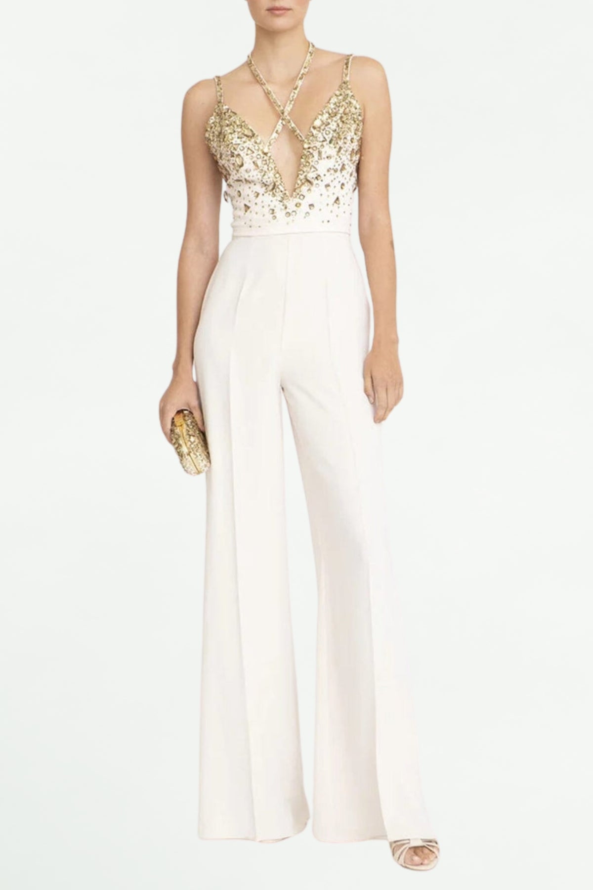 A model wearing a V-neck sequin halter jumpsuit in white, with a floral belt buckle, holding a clutch, and wearing heels.