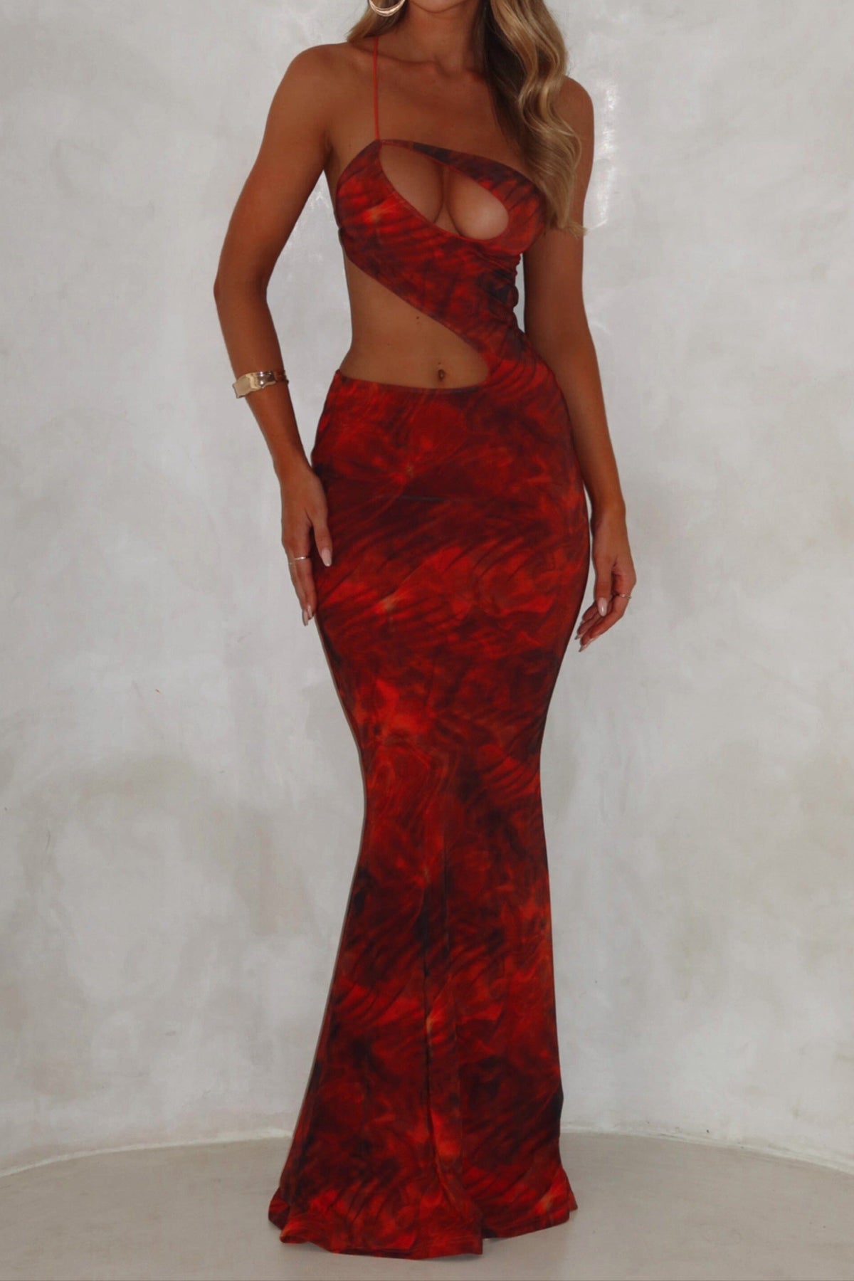A model wearing an orange maxi dress with a mesh fabrication, featuring an asymmetrical backline and an exclusive print.