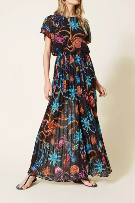 A model wearing a long pleated georgette jumpsuit with a printed design, featuring cap sleeves, an elasticated waist, and a matching fabric belt.